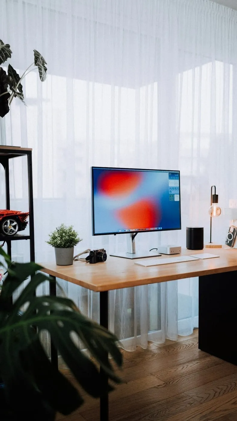A compact home office desk set against a bright curtained window in a small apartment