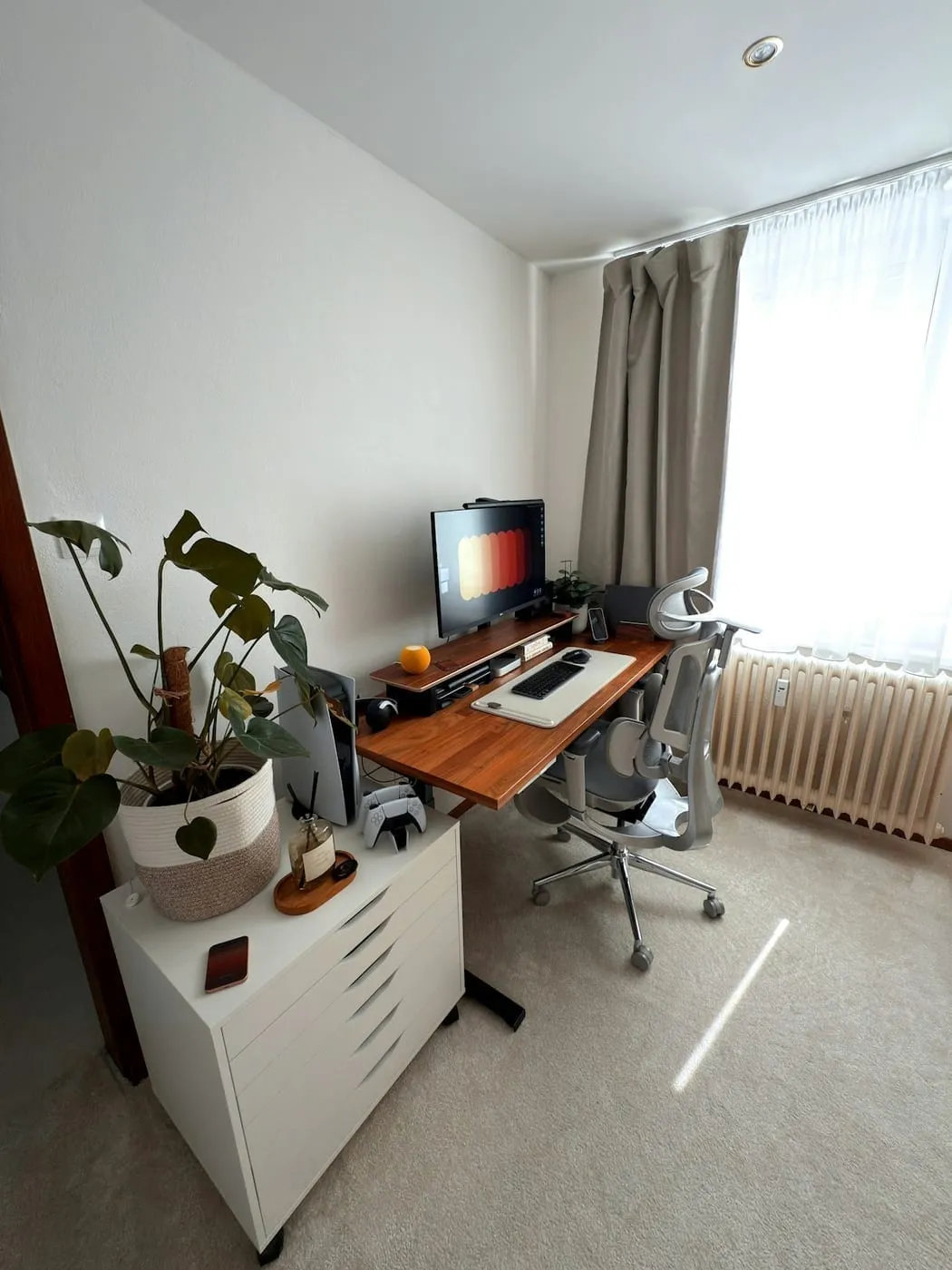 A compact desk with a rolling drawer unit beside it in a small carpeted apartment room
